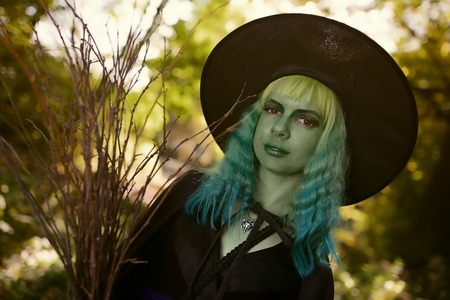 Young girl with green hair and broom in suit of witch in forest. Halloween timeの写真素材