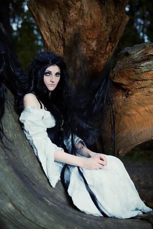 Young beautiful witch with long dark hair in root of old treeの写真素材