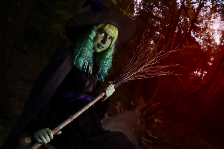 Young girl with green hair and broom in suit of witch in forest. Halloween timeの写真素材