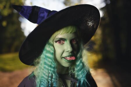 Young girl with green hair and skin suit of witch in forest. Halloween timeの写真素材