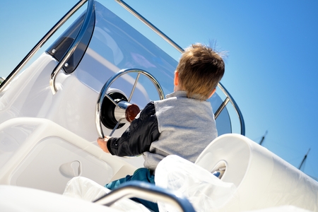 Little child sailor steering a sailboat as captainの写真素材