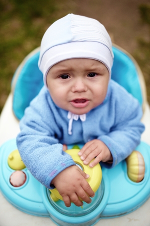 Crying cute baby in baby walker walks outdoorsの写真素材