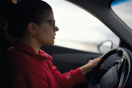 Woman wearing glasses drives car and is concentrated looks at roadの写真素材
