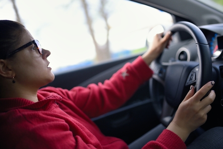 Woman wearing glasses drives car and is concentrated looks at roadの写真素材