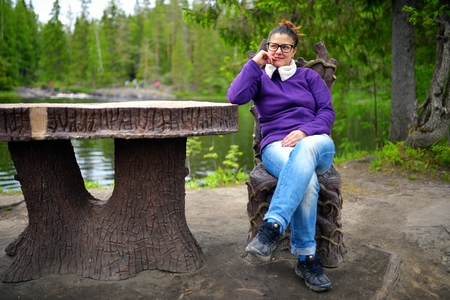 Beautiful woman sits on fairytale chair near table in wood at lakeの写真素材