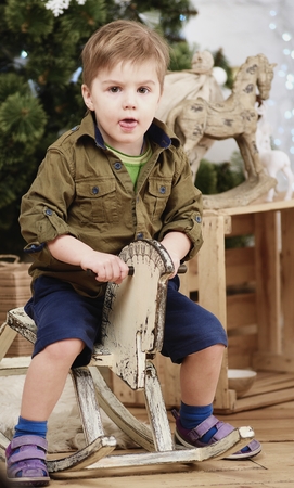 Small boy ride wooden rocking horse in front of christmas treeの写真素材