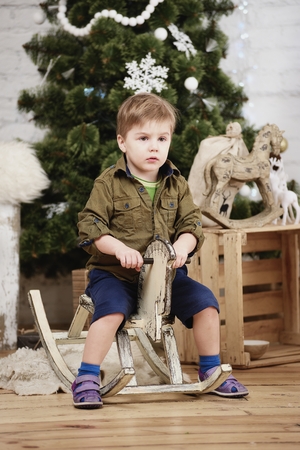 Small boy ride wooden rocking horse in front of christmas treeの写真素材