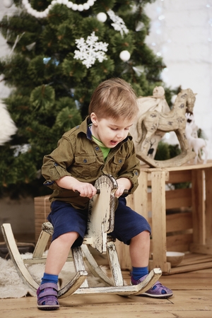 Small boy ride wooden rocking horse in front of christmas treeの写真素材