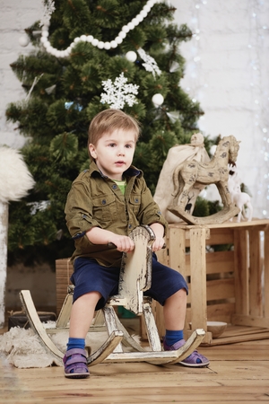 Small boy ride wooden rocking horse in front of christmas treeの写真素材