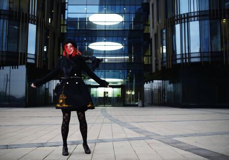 Portrait of stylish young happy woman in black coat and hat against modern buildingの写真素材