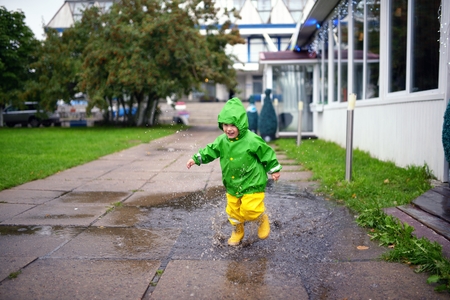 Happy little boy in not getting wet clothes plays in pool on streetの写真素材