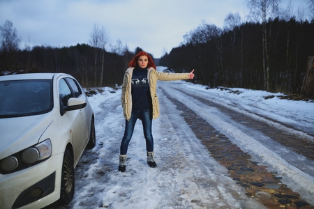 Beautiful redhead woman hitchhiking by broken carの写真素材
