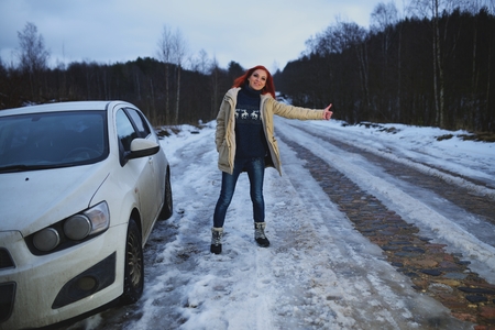 Beautiful redhead woman hitchhiking by broken carの写真素材