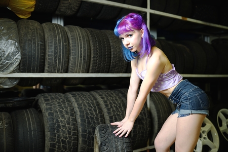 Beautiful hipster girl automobile mechanic works with tires on wheelsの写真素材