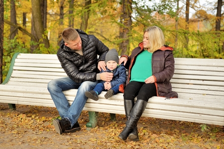 Family sits in autumn park on benchの写真素材