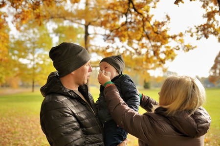 Mother wipes face scarf to child who sits on hands at fatherの写真素材