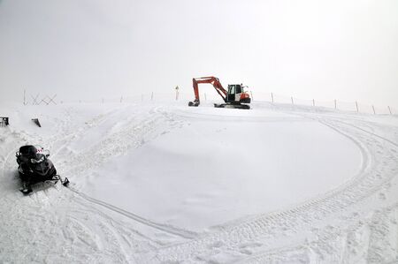 Tracklaying excavator at top of snow mountainの写真素材