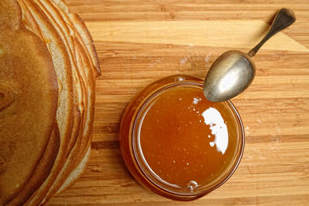 Pancakes and jar of honey with a spoon on a wooden boardの写真素材