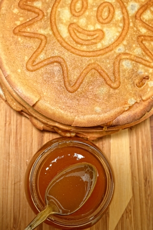 Pancakes and jar of honey with a spoon on a wooden boardの写真素材