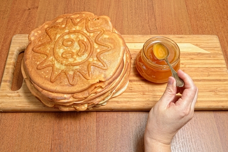 Female hand takes spoon honey from glass jar and puts on pancakesの写真素材