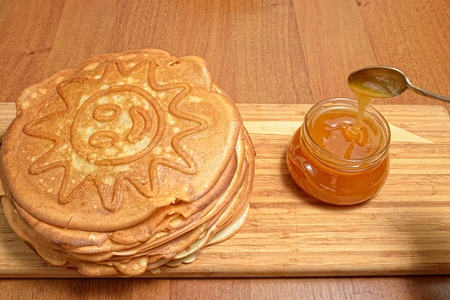 Pancakes and jar of honey with a spoon on a wooden boardの写真素材