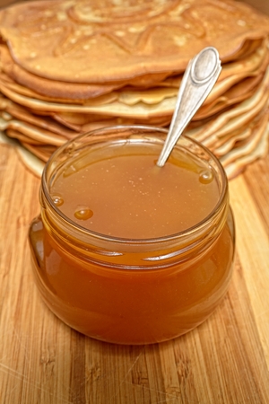 Pancakes and jar of honey with a spoon inside on a wooden boardの写真素材