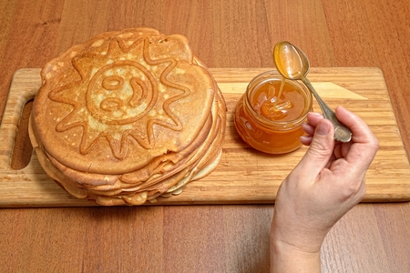Female hand takes spoon honey from glass jar and puts on pancakesの写真素材