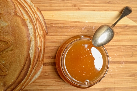 Pancakes and jar of honey with a spoon on a wooden boardの写真素材
