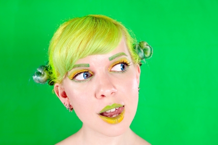 Beautyful young woman with green hair licking her lip on green background