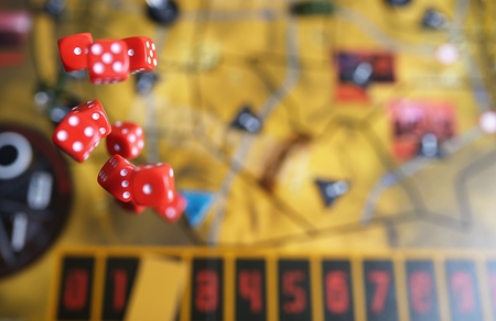 Several rolling red dice fall on a table with boardgame. Gameplay moments