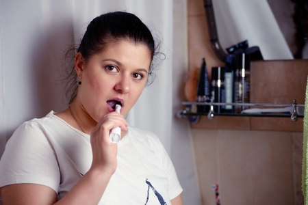 Young woman brushes teeth in bathroom an electric brushの写真素材