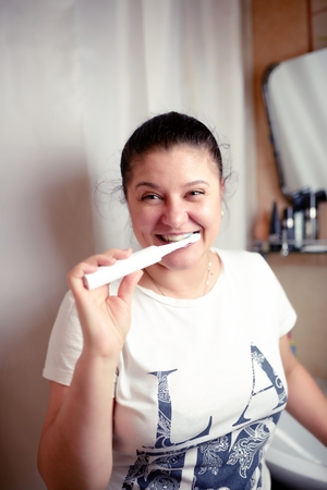 Young woman brushes teeth in bathroom an electric brushの写真素材
