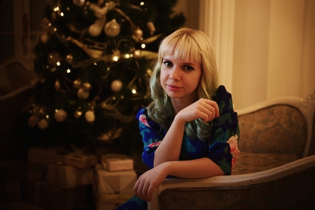 Beautiful young girl sits on sofa near Christmas tree with presentsの写真素材