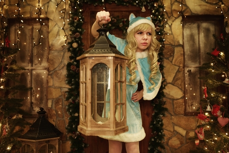 Snow Maiden holds lantern on doorstep of house decorated in Christmas styleの写真素材