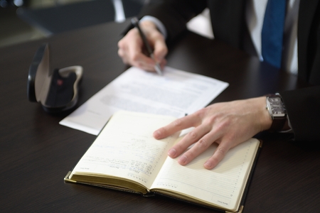 Businessman hands with pen writing notebook on office desk tableの写真素材