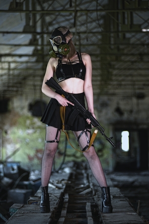 Beautiful, young girl post apocalypse girl stand in abandoned factory with gas mask and machine gunの写真素材