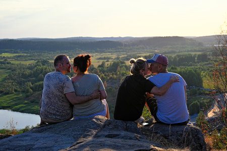 Four friends sitting on edge of mountain at sunsetの写真素材