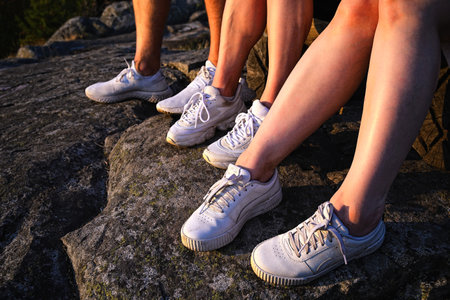 Close up view of three pairs of legs in white sneakers in nature at sunsetの写真素材