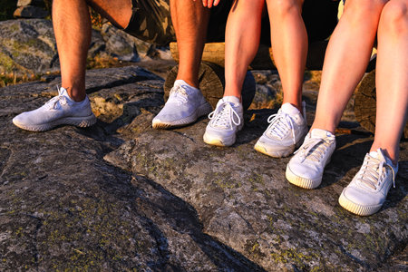 Close up view of three pairs of legs in white sneakers in nature at sunsetの写真素材