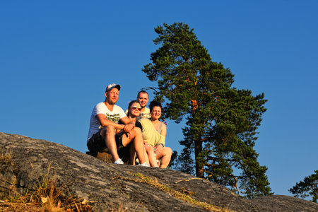 Four friends sitting on edge of mountain at sunsetの写真素材