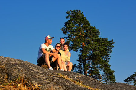 Four friends sitting on edge of mountain at sunsetの写真素材