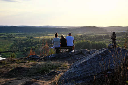 Three friends sitting on edge of mountain at sunsetの写真素材