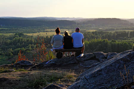 Three friends sitting on edge of mountain at sunsetの写真素材