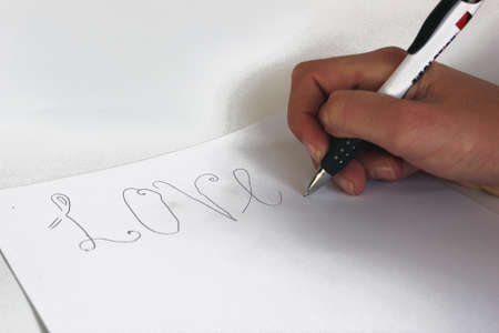 Young white girl's hand holding pen writing the word Love on white piece of paper