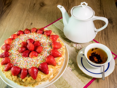 honey cake with strawberry on top and tea on wooden tableの写真素材