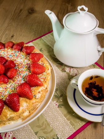 honey cake with strawberry on top and tea on wooden tableの写真素材