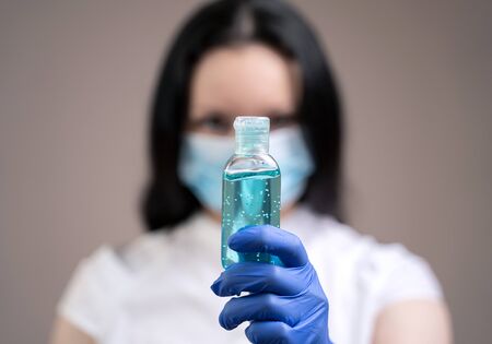Alcohol gel to protect hands from viruses is demonstrated by a girl in a protective mask and medical peppers. The concept of countering the spread of caronovirus.の写真素材