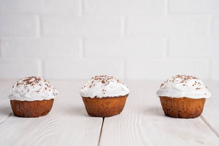 Cupcakes with whipped cream and chocolate chips on a white wooden table. Image for the menu or...