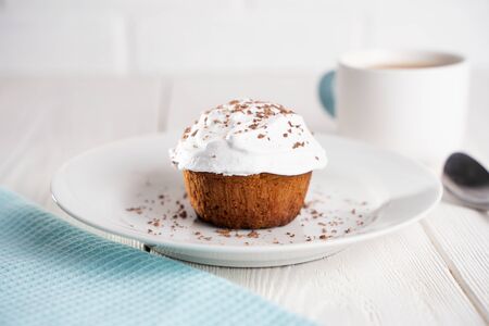 Cupcakes with whipped cream and chocolate chips on a white plate and a Cup of coffee in the...