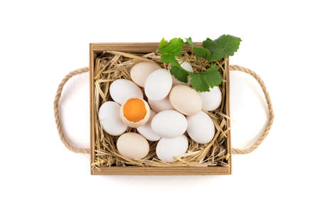 White and brown chicken eggs with a broken egg in the center, which shows a fresh yolk and a green...